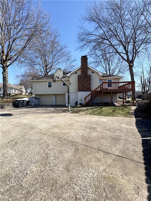 view of property exterior featuring stairway, a wooden deck, concrete driveway, a chimney, and an attached garage