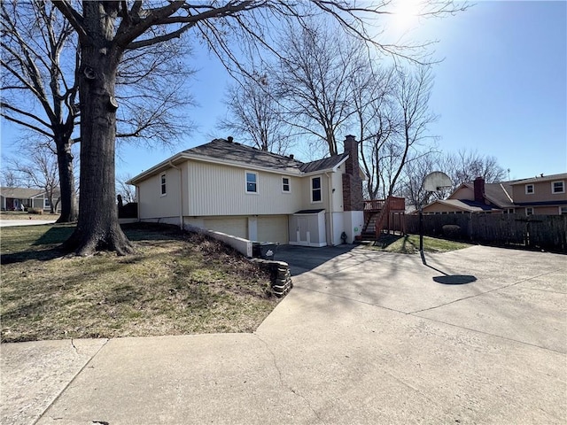 view of property exterior featuring a garage, concrete driveway, a chimney, and fence