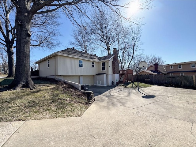 view of home's exterior with a chimney, concrete driveway, a garage, and fence