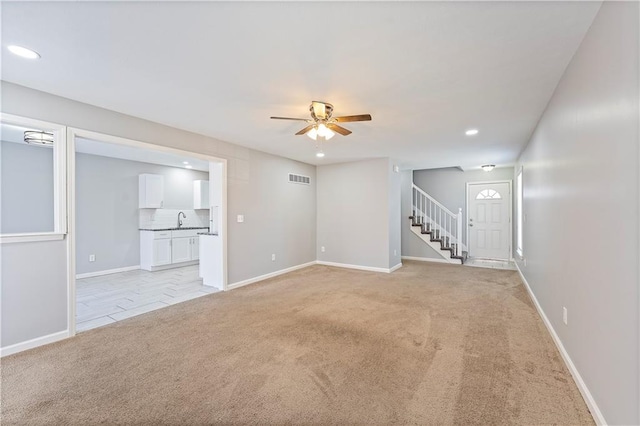 unfurnished living room featuring visible vents, baseboards, stairs, light carpet, and a ceiling fan