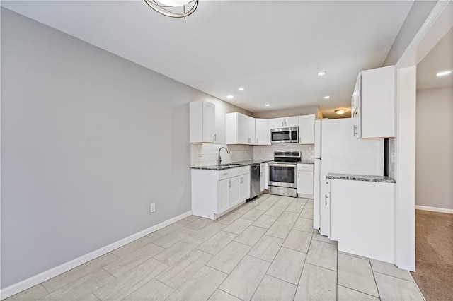 kitchen featuring dark stone counters, decorative backsplash, appliances with stainless steel finishes, white cabinetry, and a sink