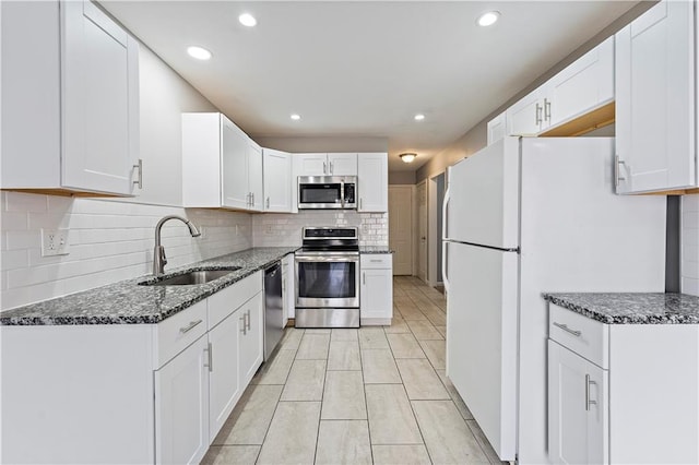 kitchen with a sink, dark stone counters, appliances with stainless steel finishes, and white cabinets