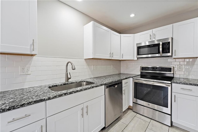 kitchen with dark stone counters, a sink, stainless steel appliances, white cabinetry, and backsplash