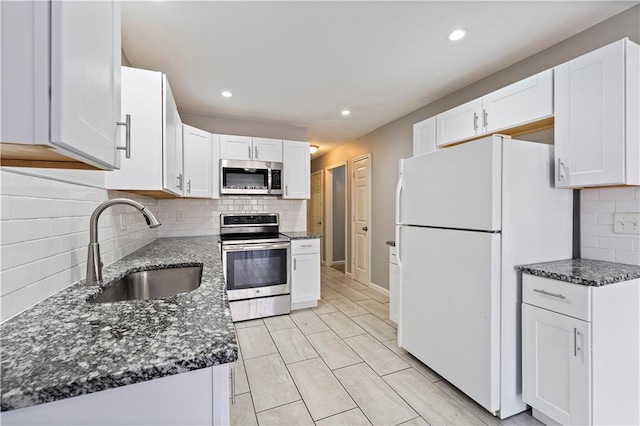 kitchen featuring dark stone countertops, recessed lighting, a sink, stainless steel appliances, and white cabinetry