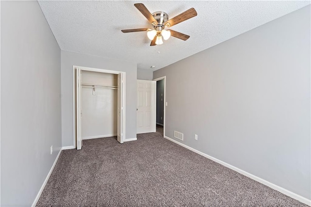 unfurnished bedroom with visible vents, a textured ceiling, a closet, dark colored carpet, and baseboards