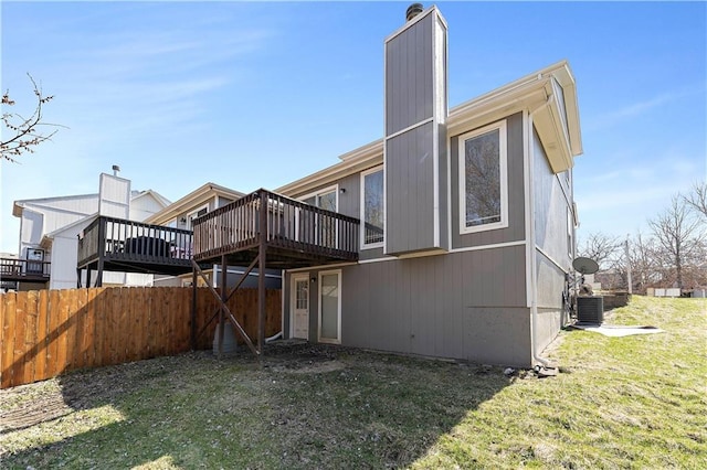 rear view of property featuring fence, a wooden deck, central AC unit, a lawn, and a chimney