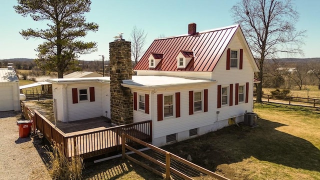 back of property featuring fence, a standing seam roof, a yard, a chimney, and metal roof