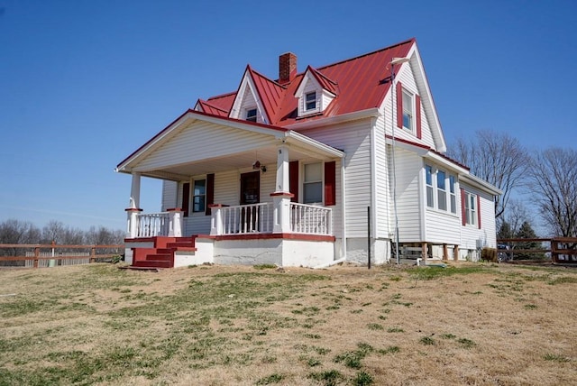 view of front facade featuring fence, covered porch, a front yard, metal roof, and a chimney