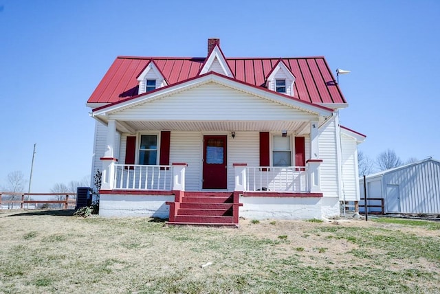 view of front of house featuring covered porch, central AC, a chimney, a front lawn, and metal roof