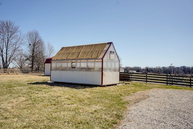 view of greenhouse with a rural view, a lawn, and fence