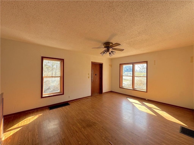 empty room featuring visible vents, a textured ceiling, baseboards, and wood finished floors