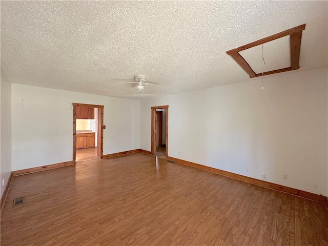 empty room with light wood-type flooring, attic access, ceiling fan, and visible vents