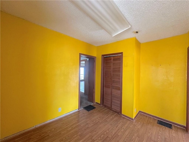 unfurnished bedroom with visible vents, a textured ceiling, wood finished floors, a closet, and baseboards