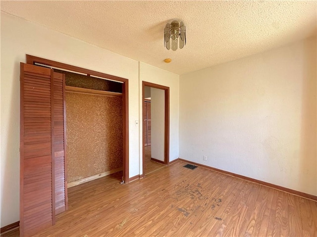 unfurnished bedroom with visible vents, baseboards, wood finished floors, a closet, and a textured ceiling