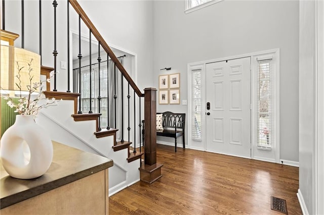 entrance foyer featuring stairway, wood finished floors, visible vents, baseboards, and a towering ceiling