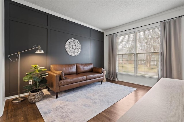 living room with wood finished floors, a textured ceiling, ornamental molding, and a decorative wall