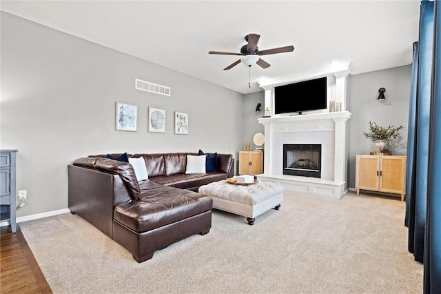 carpeted living room with visible vents, a tile fireplace, baseboards, and a ceiling fan