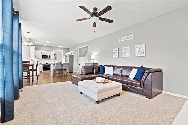 carpeted living area featuring visible vents, ceiling fan with notable chandelier, a textured ceiling, and baseboards