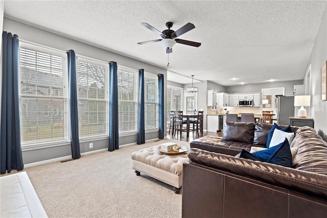 living room with baseboards, light carpet, a textured ceiling, and ceiling fan