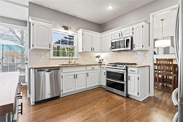 kitchen with a sink, light stone counters, dark wood-style floors, white cabinetry, and stainless steel appliances