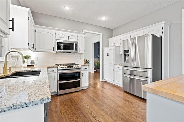 kitchen featuring light stone counters, dark wood-style floors, a sink, decorative backsplash, and appliances with stainless steel finishes