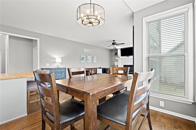 dining area featuring visible vents, baseboards, ceiling fan with notable chandelier, a fireplace, and wood finished floors