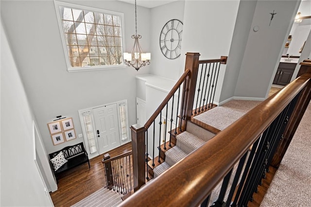 stairway with baseboards, an inviting chandelier, and wood finished floors