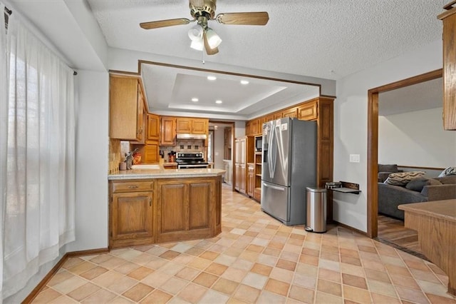 kitchen with a tray ceiling, tasteful backsplash, appliances with stainless steel finishes, a peninsula, and light countertops