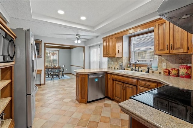 kitchen with a wealth of natural light, a tray ceiling, stainless steel appliances, a peninsula, and light countertops