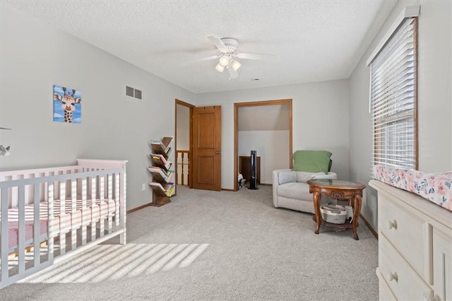 carpeted bedroom with visible vents, a crib, a textured ceiling, and baseboards