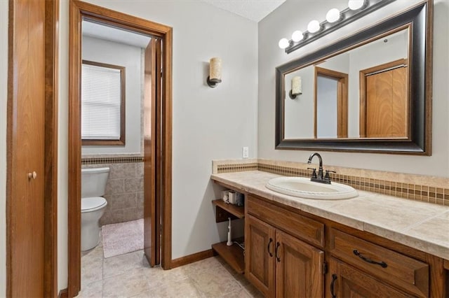 bathroom with tile patterned flooring, tile walls, a wainscoted wall, toilet, and vanity