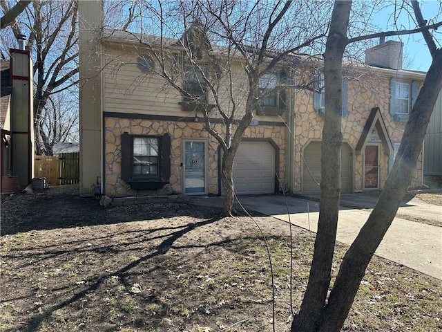 view of front facade with an attached garage, fence, stone siding, and driveway