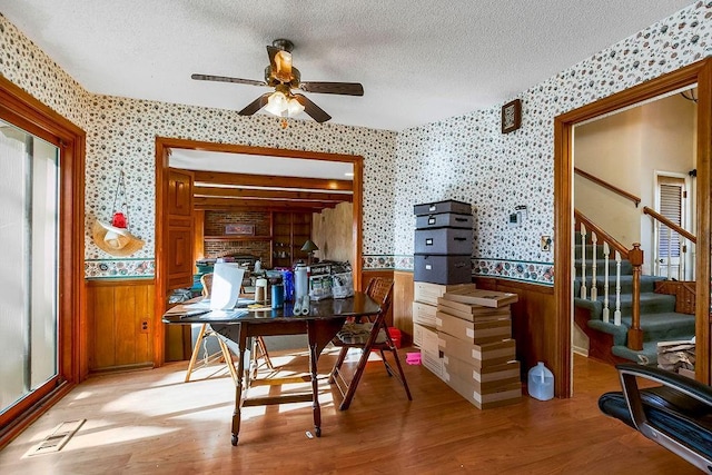 home office with a wainscoted wall, a textured ceiling, and wallpapered walls