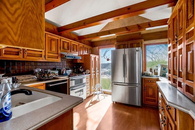 kitchen with under cabinet range hood, dishwasher, double oven range, brown cabinets, and freestanding refrigerator