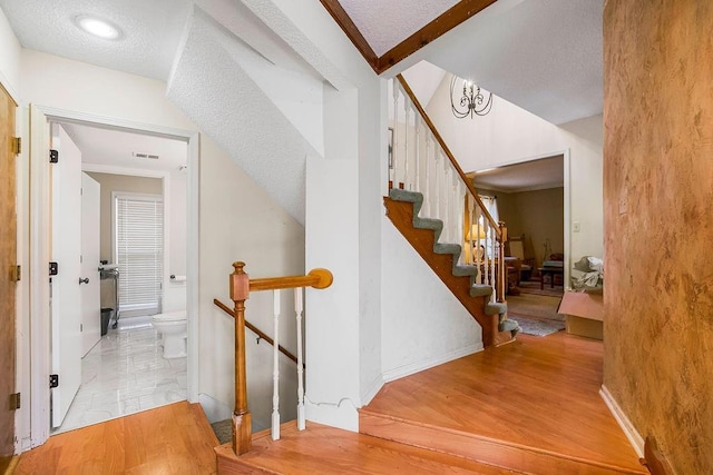 stairs featuring baseboards, wood finished floors, visible vents, and a textured ceiling