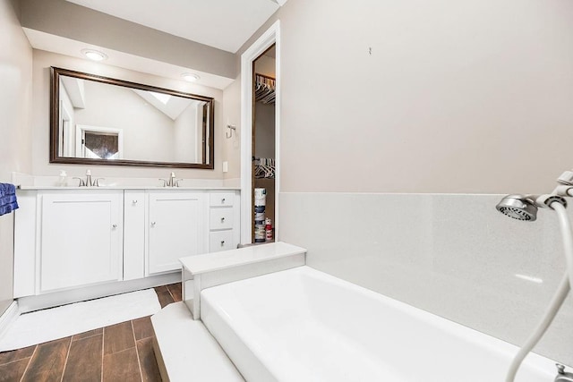 bathroom featuring a walk in closet, wood finish floors, double vanity, vaulted ceiling, and a sink