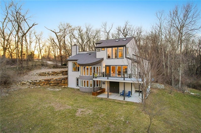 back of house featuring roof with shingles, stucco siding, a chimney, a yard, and a patio area