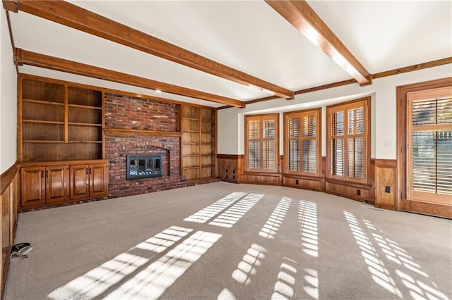 unfurnished living room featuring beam ceiling, a brick fireplace, light colored carpet, and a wainscoted wall