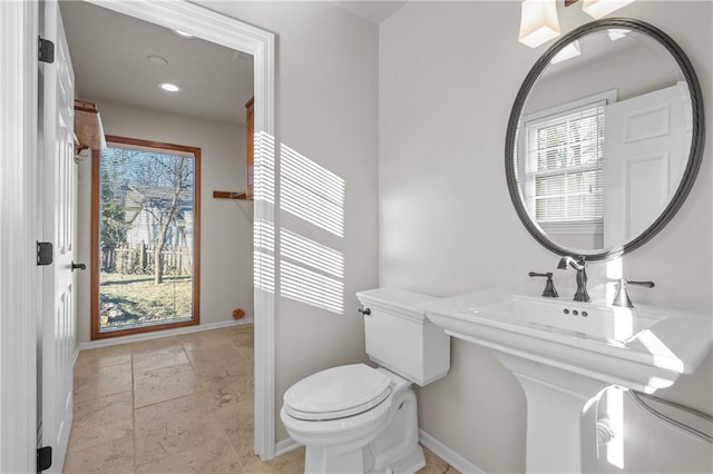 half bathroom with stone tile floors, toilet, and baseboards