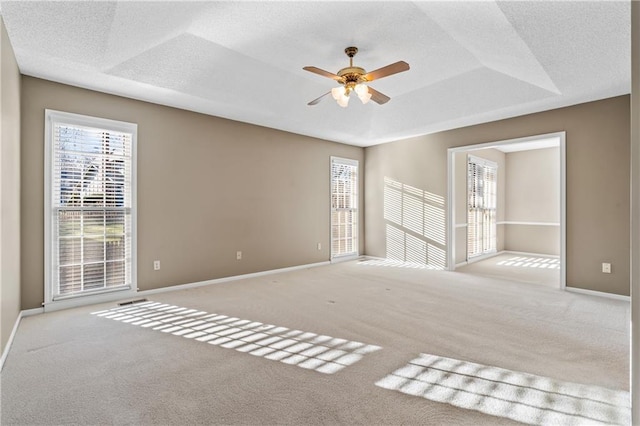 carpeted empty room with a ceiling fan, a raised ceiling, a healthy amount of sunlight, and a textured ceiling