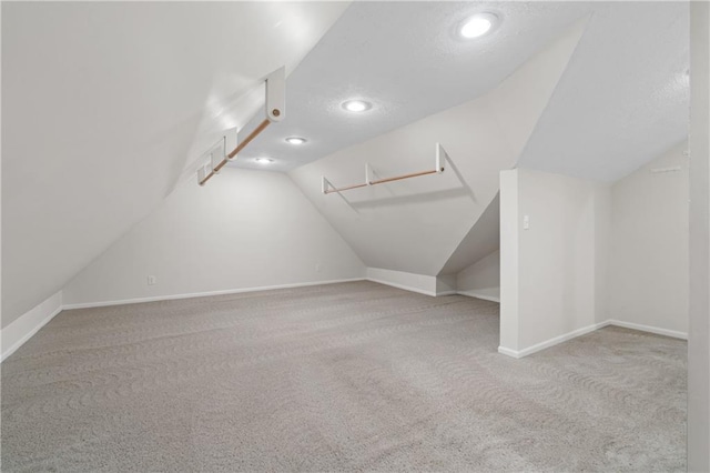 additional living space with carpet floors, a textured ceiling, baseboards, and vaulted ceiling