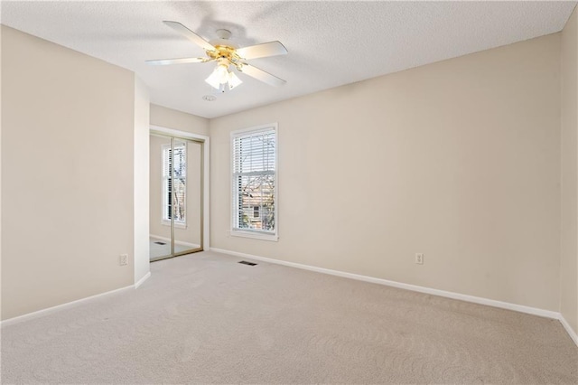 carpeted spare room with baseboards, visible vents, a textured ceiling, and ceiling fan