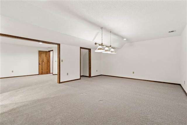 empty room featuring a textured ceiling, lofted ceiling, baseboards, and light carpet