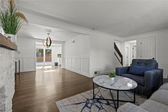 living room featuring a notable chandelier, a textured ceiling, wood finished floors, a decorative wall, and stairs