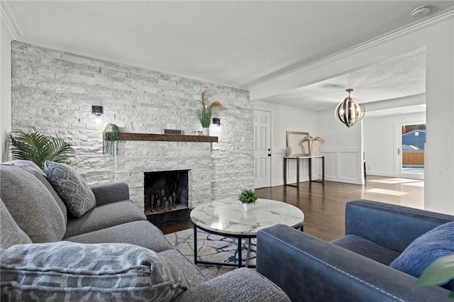 living room with ornamental molding, a stone fireplace, an inviting chandelier, wood finished floors, and a decorative wall