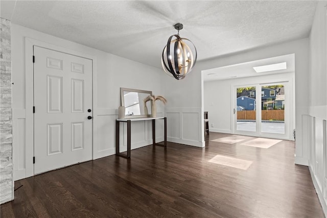 foyer entrance with wood finished floors, a textured ceiling, a chandelier, and a decorative wall