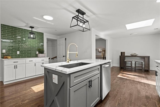 kitchen with a skylight, dark wood-style flooring, gray cabinetry, a sink, and dishwasher