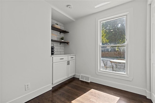 interior space featuring dark wood-style floors, visible vents, a bar, and baseboards