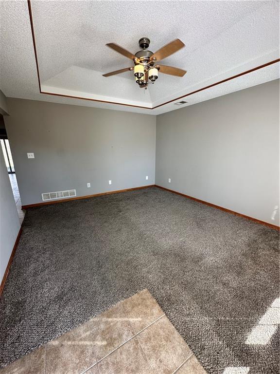 carpeted empty room with visible vents, a textured ceiling, and a tray ceiling