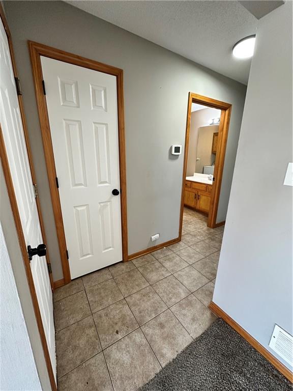 corridor with light tile patterned floors, visible vents, baseboards, and a textured ceiling